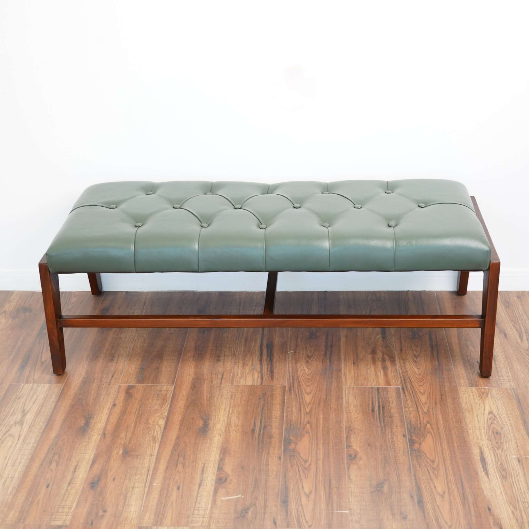 A green leather bench with button detailing, set on a solid walnut wood frame.