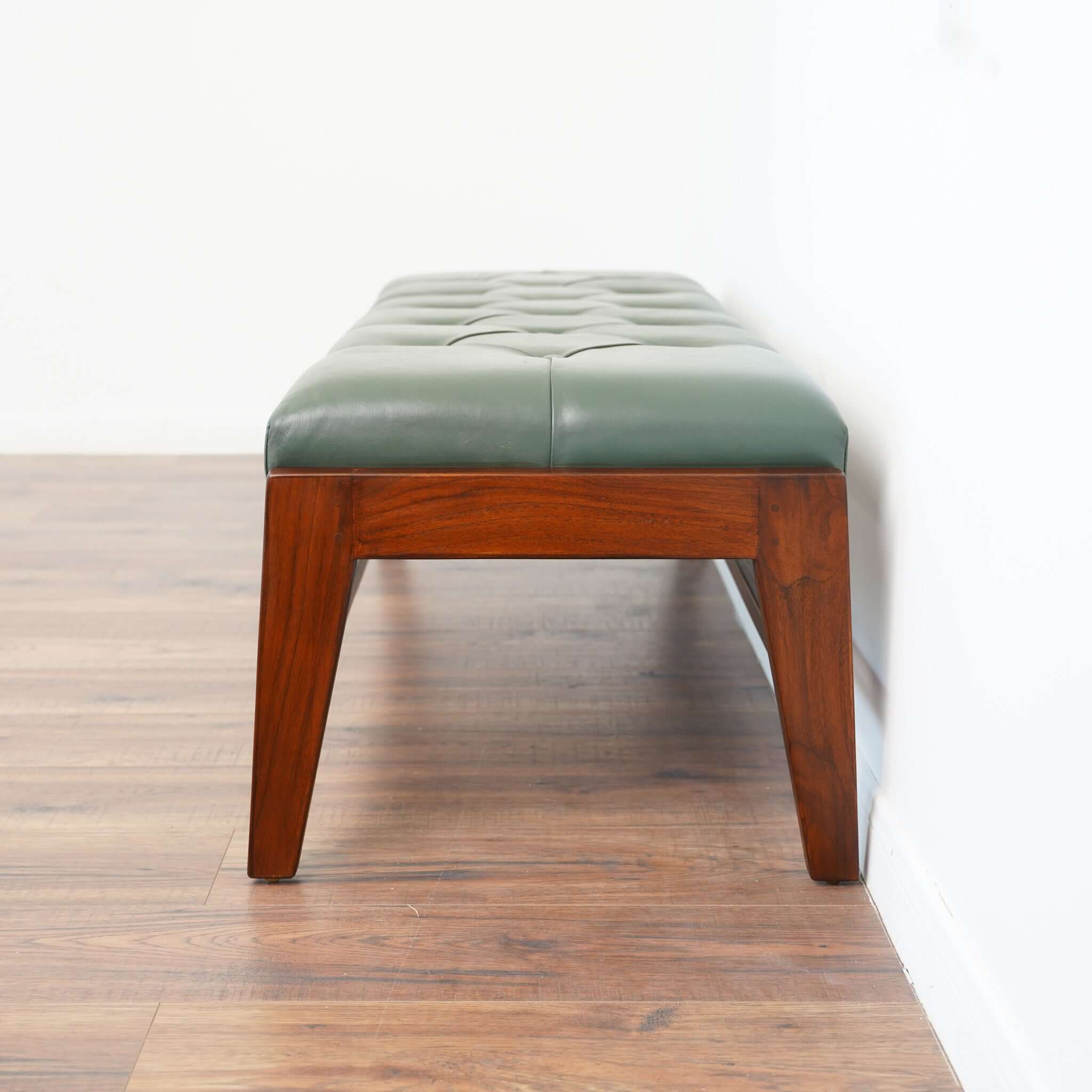 A green leather bench with button detailing, set on a solid walnut wood frame.