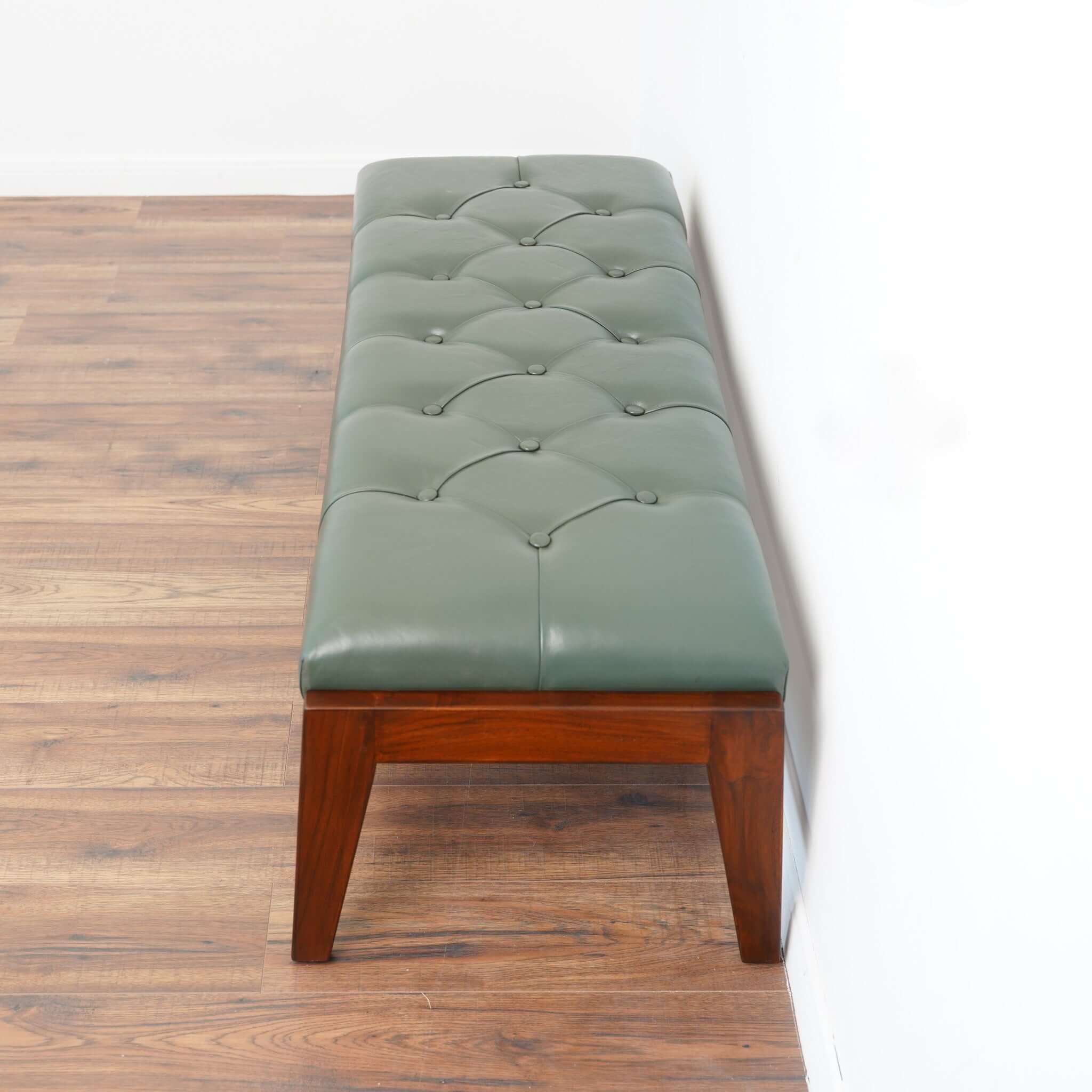 A green leather bench with button detailing, set on a solid walnut wood frame.